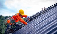 Roofer worker in protective uniform wear and gloves, using air or pneumatic nail gun and installing asphalt shingle on top of the new roof,Concept of residential building under construction.
